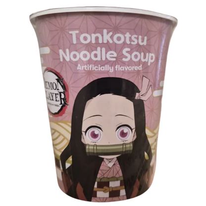 A pink cup of instant soup featuring Demon Slayer theme packaging labeled "Tonkotsu Noodle Soup - Artificially flavored" at the top. Centered on the front is an anime illustration of Nezuko Kamado with her large pink eyes, pink ribbon, and bamboo muzzle, set against a pink hemp-leaf geometric pattern background. The "Demon Slayer: Kimetsu no Yaiba" logo is printed on the left side.